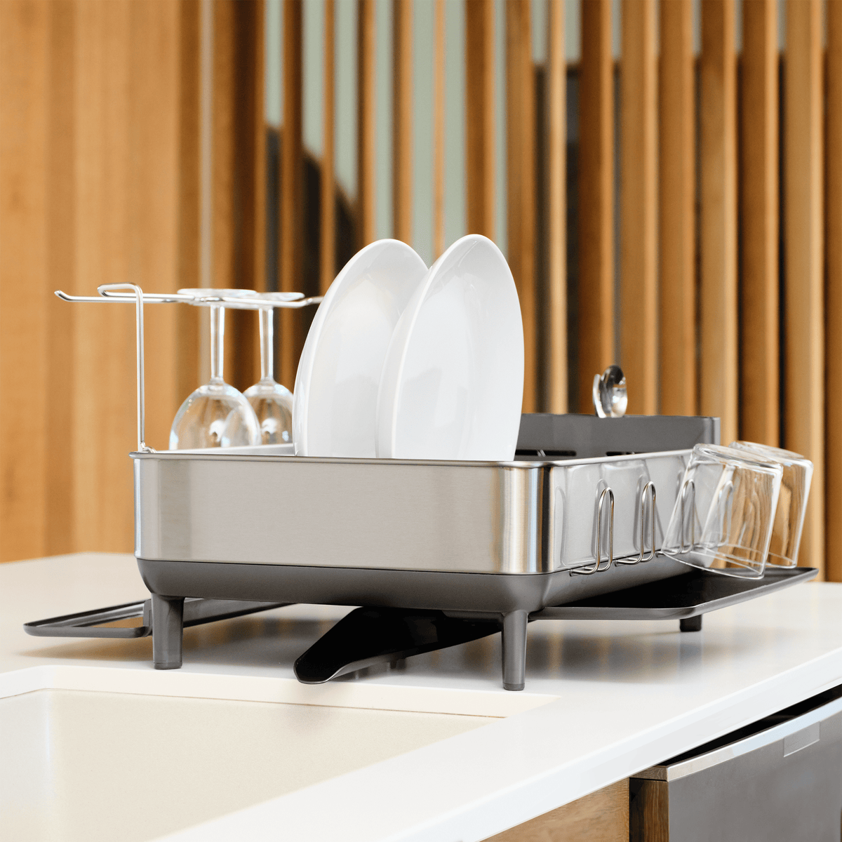 Simplehuman Brushed Stainless Steel Steel Frame Dishrack angled view on a countertop, drying plates and wine glasses with integrated drainage.