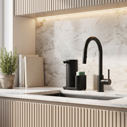 Simplehuman's 14 oz. Liquid Sensor Pump in Matte Black in a modern kitchen setting with marble countertops, books and small plants lining the counter and light wooden colored cabinets.
